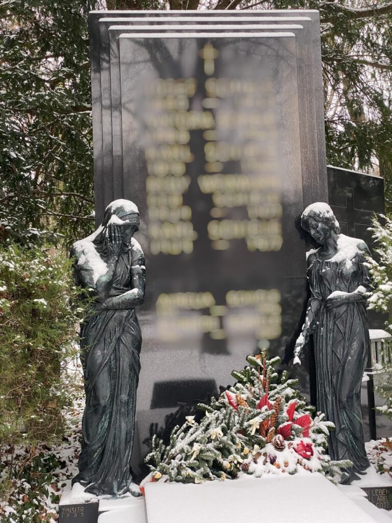 Verschneite Grabstätte am Wiener Zentralfriedhof mit zwei steinernen, weiblichen Figuren, die anhand ihrer Pose Trauer ausdrücken. 