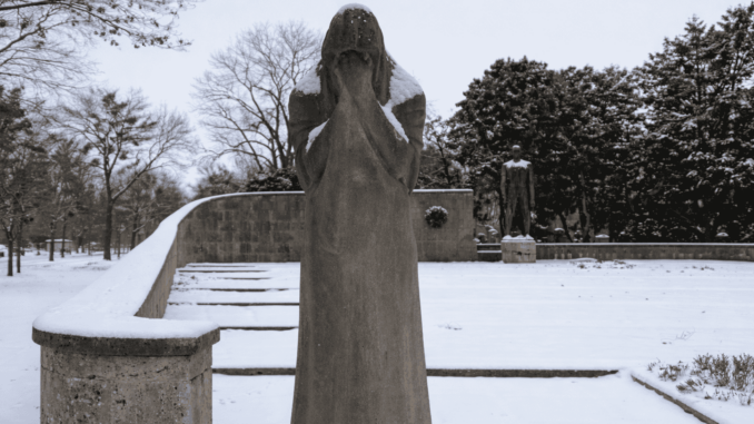 Allegorische Darstellung im Vollbild einer trauernden Frau, die sich die Hände ins Gesicht hält am verschneiten Mahnmal gegen Faschismus am Zentralfriedhof.